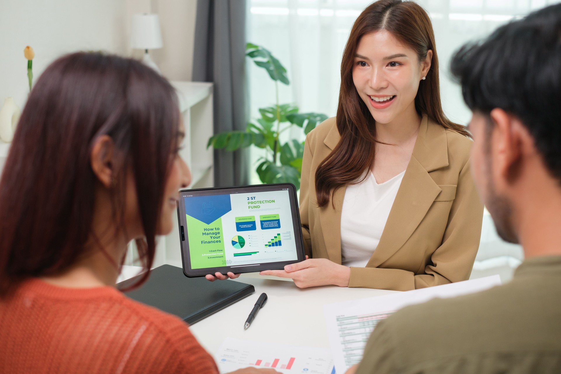 asian financial advisor presenting charts and data on a tablet during couple client meeting.financial planning and decision-making